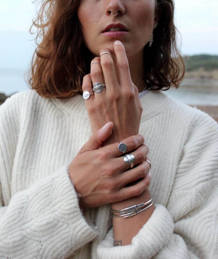Portrait of Adrienne framed cutting just above her nose, showing her hands with jewellery, and wearing a white jumper