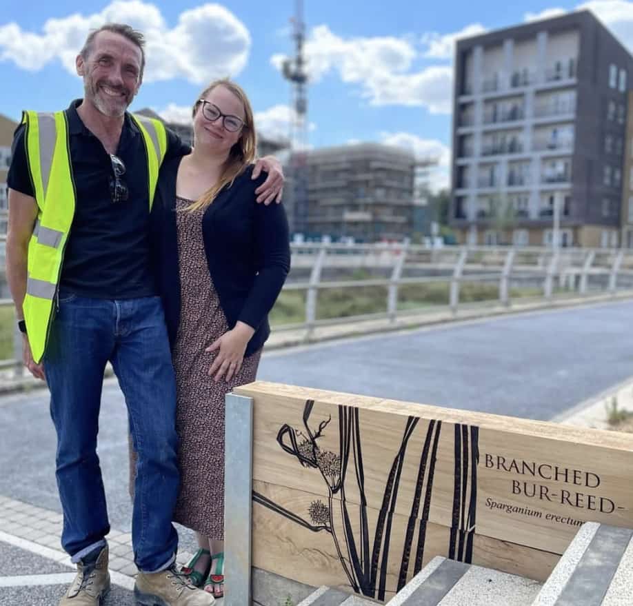 full length image of Kim and her husband standing next to a wooden bench Installation outside some industrial buildings