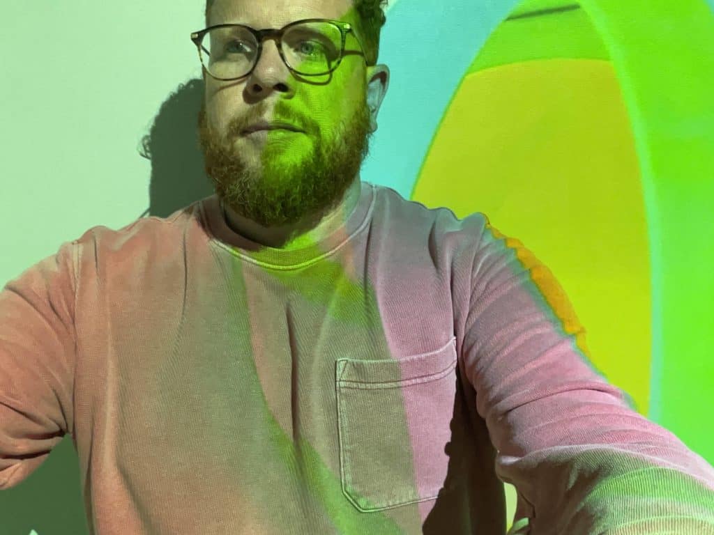 Portrait of Sean wearing glasses against a blue and green background